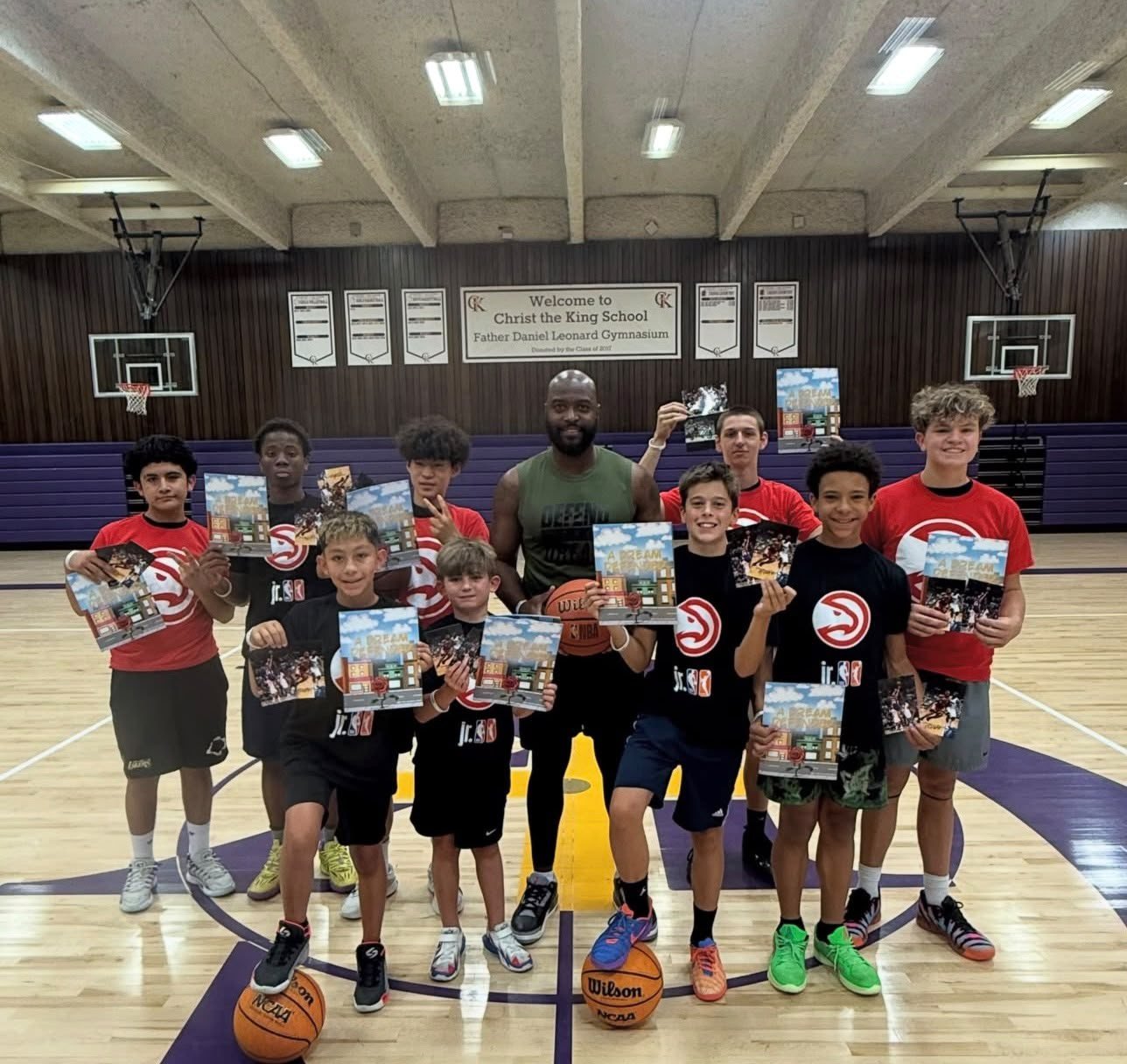 Mario West with Jr. NBA players at Christ the King School holding copies of A Dream Defended